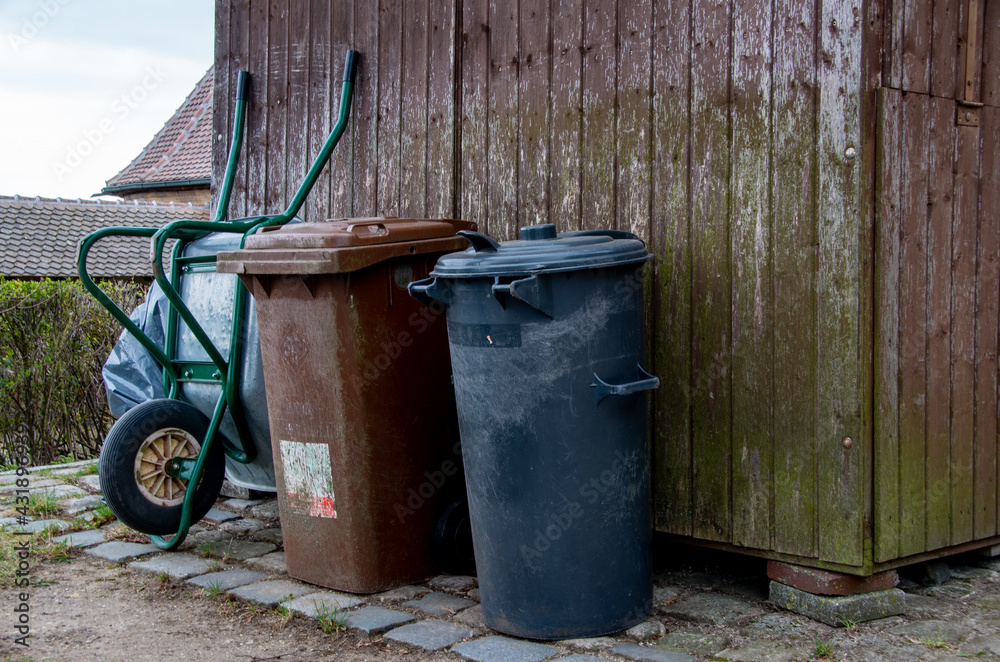 Obraz premium Garbage cans and a wheelbarrow lean against a wooden shed