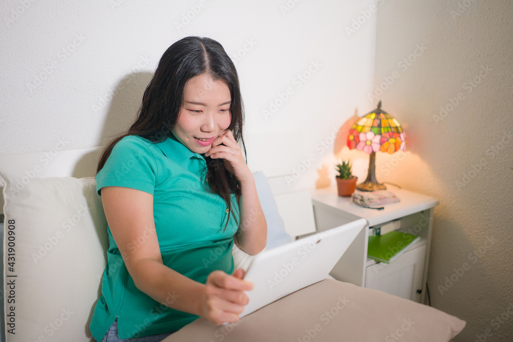 young happy and attractive Asian Japanese woman at home networking or studying using digital tablet on bed relaxed and cheerful in internet communication