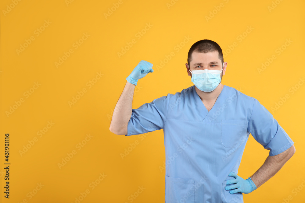Doctor with protective mask showing muscles on yellow background, space for text. Strong immunity concept Doctor with protective mask showing muscles on yellow background, space for text. Strong immunity concept