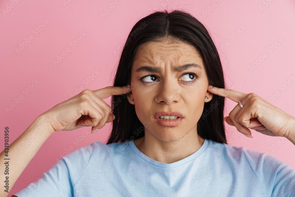 Young displeased woman plugging her ears and frowning Young displeased woman plugging her ears and frowning