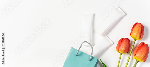 Set of cosmetic unbranded containers in paper bag and bright tulips on white background long banner format. Cosmetic sale banner. Spring and summer cosmetic sale. Skin care products.