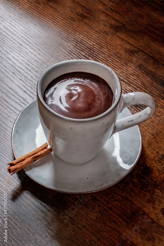Hot chocolate in a cup, with a cinnamon stick, on a rustic wooden background