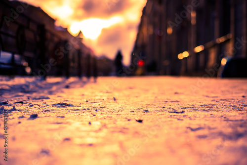 Bright winter sun in a big city, a pedestrian distance walking on a snowy street. Close up view from the level of the sidewalk near the fence