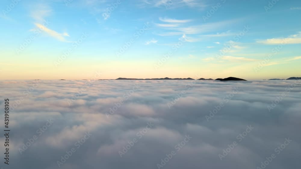 Aerial view of vibrant sunset over white dense clouds with distant dark mountains on horizon. Aerial view of vibrant sunset over white dense clouds with distant dark mountains on horizon.