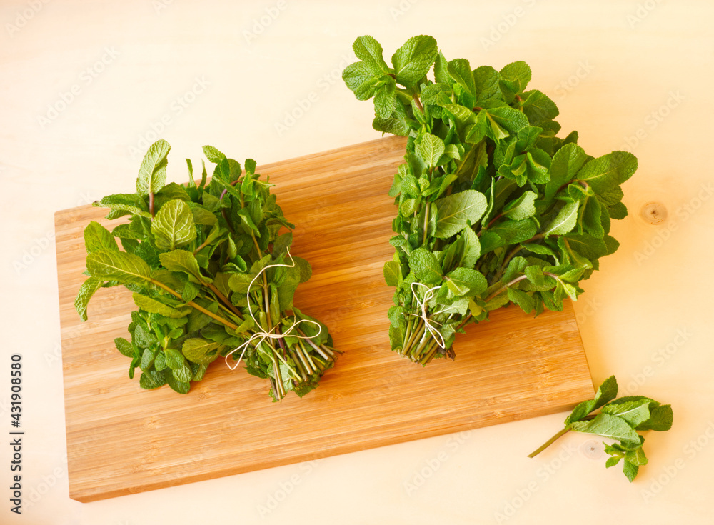 Bunches of fresh mint on wooden table. Green small courgette in wire basket. Brown carving wooden board. Fresh herbs for cooking or mint tea. Bunches of fresh mint on wooden table. Green small courgette in wire basket. Brown carving wooden board. Fresh herbs for cooking or mint tea.