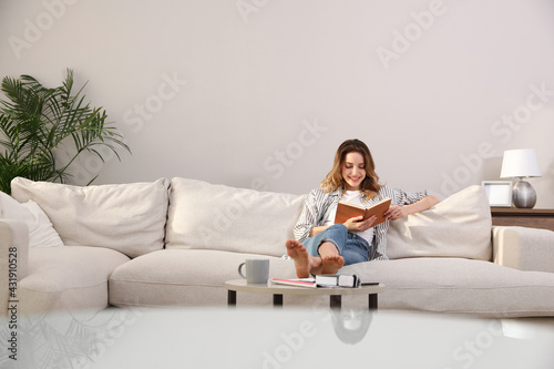 Fotografie Young woman reading book on sofa at home