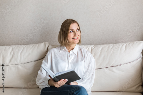 Woman is sitting on the couch holding a book in her hand.