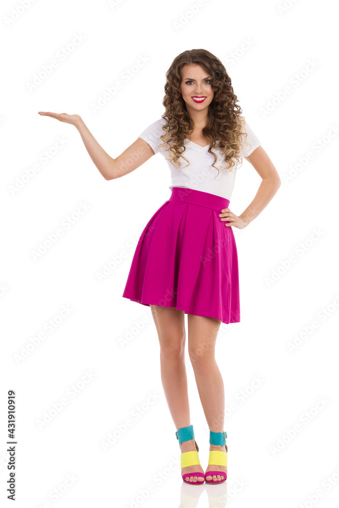 Smiling Young Woman In Colorful High Heels Is Standing With Hand Raised And Presenting Smiling Young Woman In Colorful High Heels Is Standing With Hand Raised And Presenting