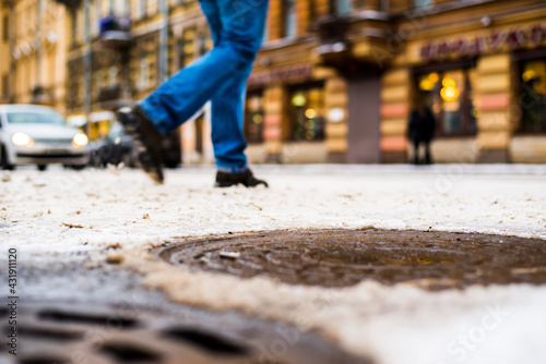 Snowy winter in the big city, a pedestrian crossing the road. Close up view of a hatches at the level of the asphalt