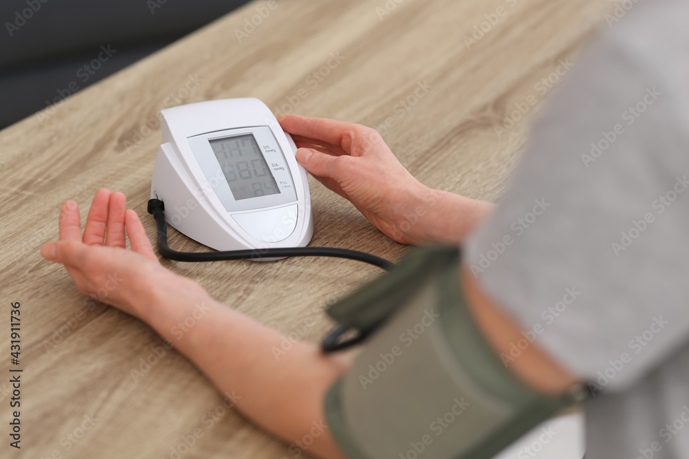 Woman checking blood pressure at wooden table indoors, closeup Woman checking blood pressure at wooden table indoors, closeup