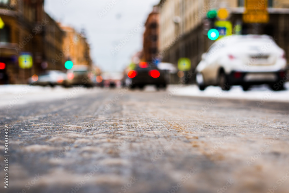 Snowy winter in the big city, the cars traveling on a green traffic light signal. Close up view from the asphalt level