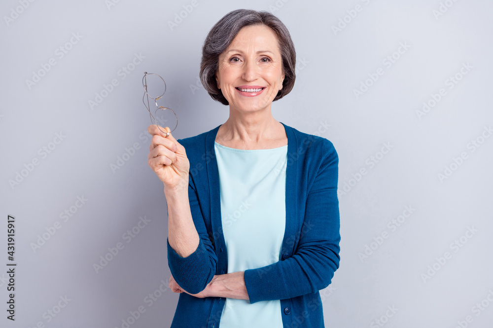 Photo portrait of happy elder woman keeping glasses wearing blue cardigan smiling isolated on grey color background Photo portrait of happy elder woman keeping glasses wearing blue cardigan smiling isolated on grey color background