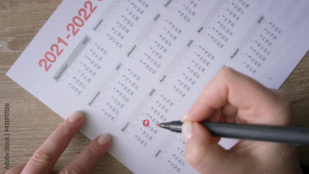 Female hands circling dates by red marker in desk calendar, making schedule Female hands circling dates by red marker in desk calendar, making schedule
