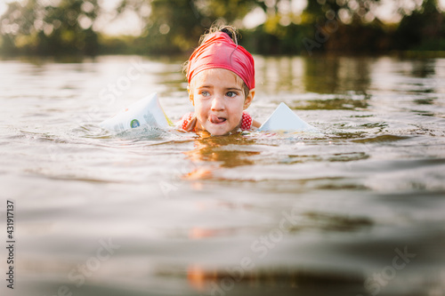 Fototapeta Naklejka Na Ścianę i Meble -  Happy summertime, healthy childhood, sport concept. Close up portrait of girl with red kerchief swimming in river in hot summer day. Soft focus. Horizontal shot.