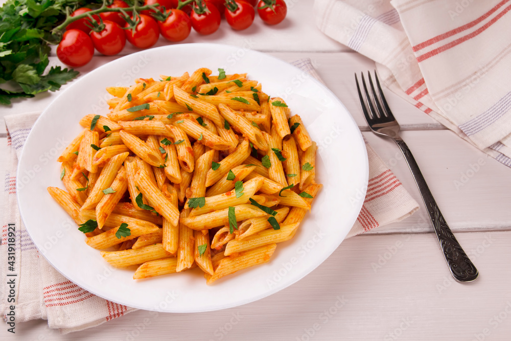 Penne pasta in tomato sauce, decorated with parsley on a white wooden table