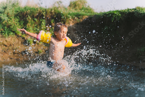 Happy summertime  healthy childhood concept. Little boy playing  splashing  jumping and having fun in a river in summer. Soft focus on splashes. Horizontal shot.