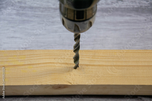 A drill with a metal drill bit drills a wooden bar.