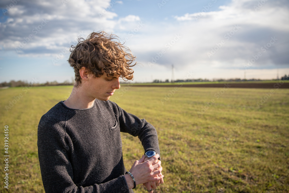 Attractive caucasian boy watches the time on his watch in a meadow.