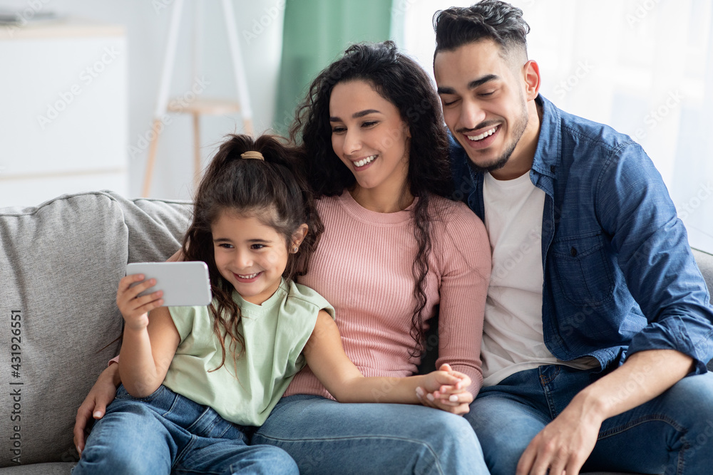 Happy Arab Family With Little Daughter Watching Videos On Smartphone At Home