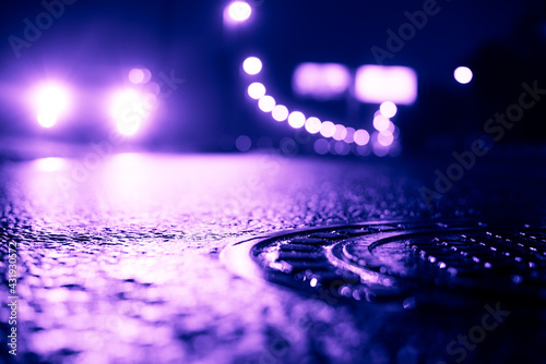 Foggy night in the big city, the headlights rushing toward the car. Close up view of a hatch at the level of the asphalt