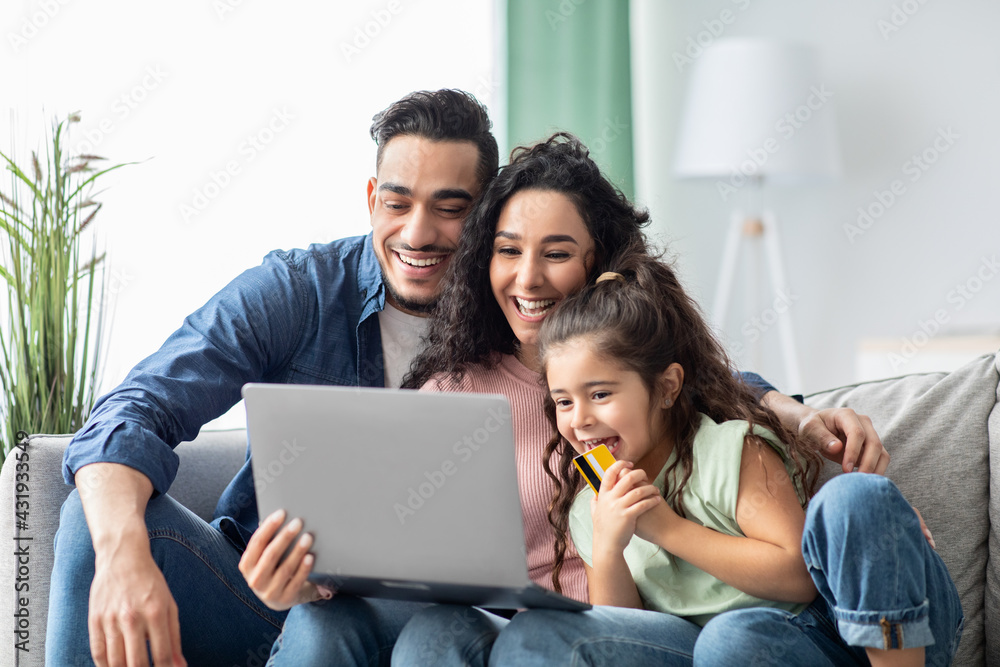 Cheerful Middle Eastern Family Shopping Online With Laptop And Card At Home Cheerful Middle Eastern Family Shopping Online With Laptop And Card At Home