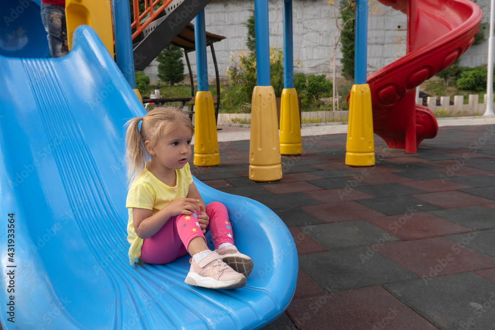 © Maria Mikhaylichenko - Caucasian child sits on a slide after riding, looking forward, colourful playground, happy childhood, summertime.