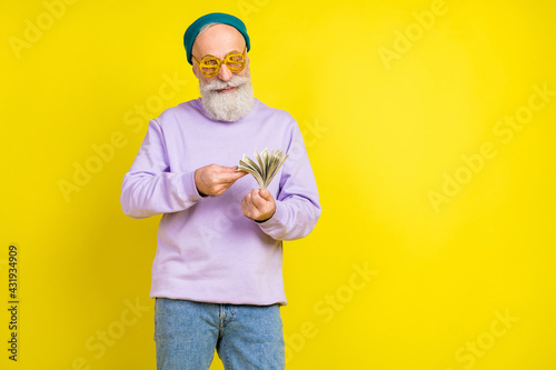 Photo of attractive pretty mature man dressed purple pullover eyewear counting money empty space isolated yellow color background
