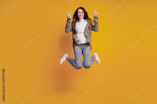 Full size photo of young cheerful woman jump show v-sign isolated on yellow background