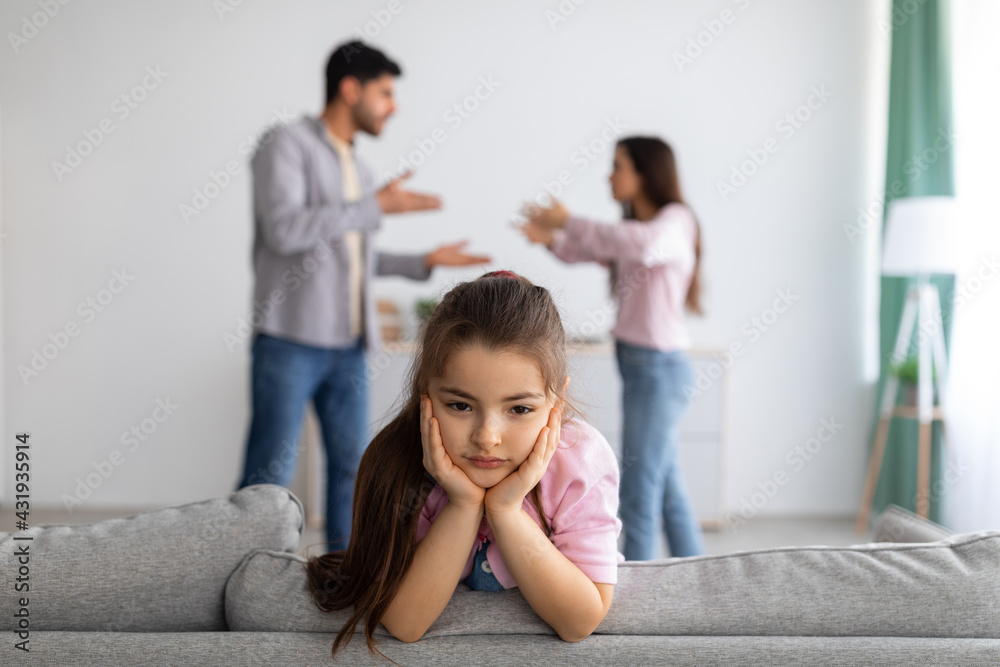Family crisis and relationship problems. Upset girl looking at camera while her angry parents fighting on the background