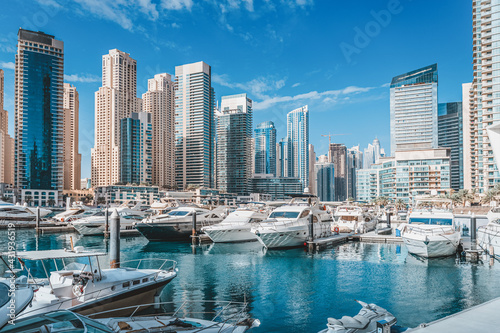 Small yacht and motor boats parking at the port near Dubai Marina Mall with row of high skyscrapers residential buildings and hotels