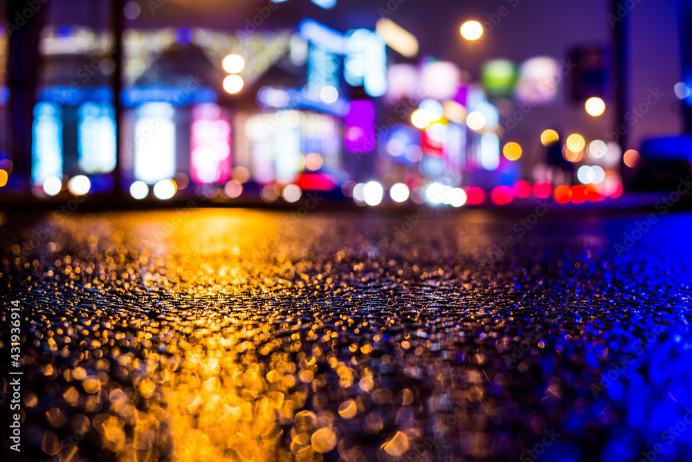 Fototapeta premium Rainy night in the big city, illumination lights of the shopping center. Close up view from the asphalt level
