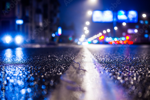 Rainy night in the big city, the road lighting lanterns and headlights of the approaching cars. Close up view from the level of the dividing line