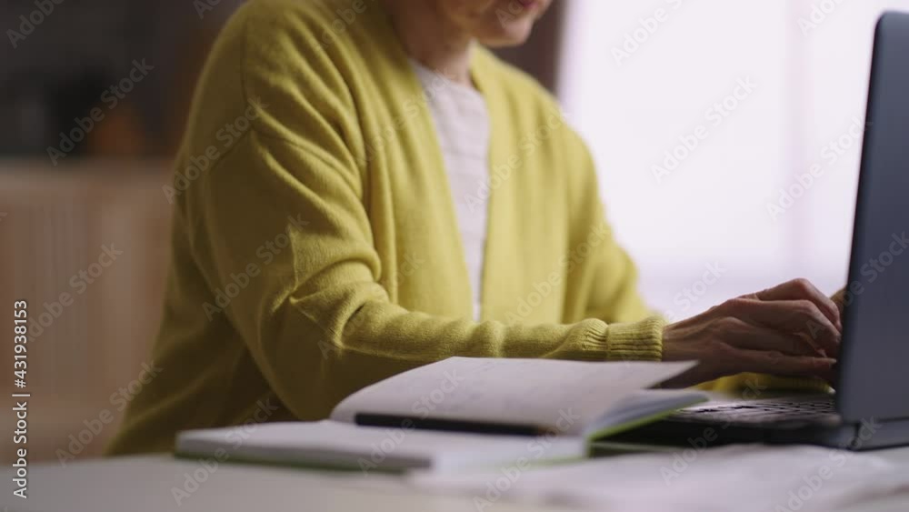 elderly woman is working with laptop and papers in home office, filling report, checking documents, closeup of hands elderly woman is working with laptop and papers in home office, filling report, checking documents, closeup of hands
