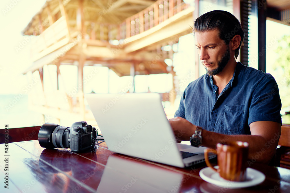 Fototapeta premium Freelance concept. Young bearded man working on laptop computer while sitting on cafe terrace.