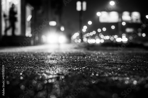 Rainy night in the big city, the car lights up the road and the man leaves home. Close up view from the sidewalk level