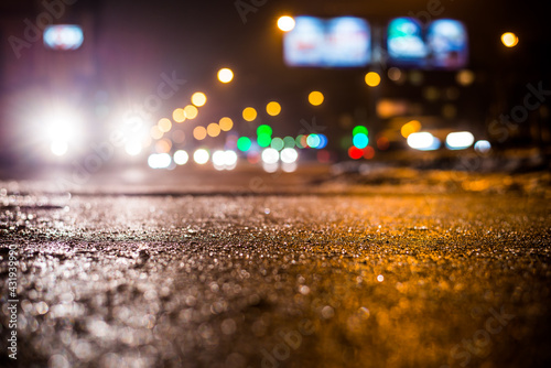 Rainy night in the big city, glare from the headlights of the parked car and a passing near the stream of cars. Close up view from the sidewalk level