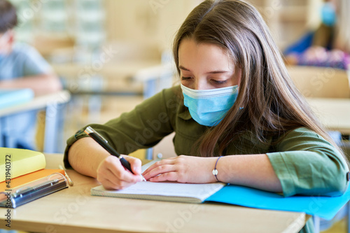 Close up of schoolgirl in protective mask writing in notebook
