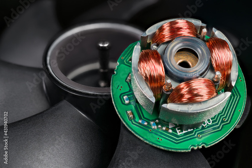 Closeup of inductors on stator and rotor with permanent magnet and black blades in background. Electric EC motor of open computer fan with copper wire on iron sheets on green electronic circuit board.