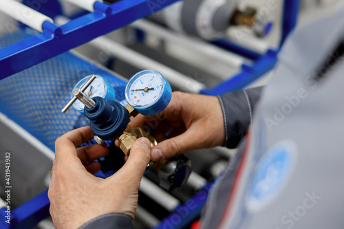 A metrology laboratory specialist takes a compressed gas cylinder for testing and verification. The man connects the pressure gauge. Analyze gas and check connections for leaks. © NEZNAEV