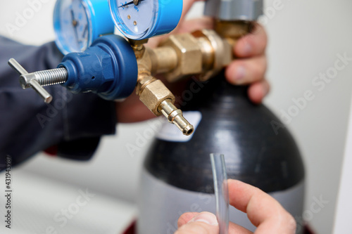 A metrology laboratory specialist takes a compressed gas cylinder for testing and calibration with a chromatograph. A man connects a hose for gas analysis. Gas analyzer and chromatography.