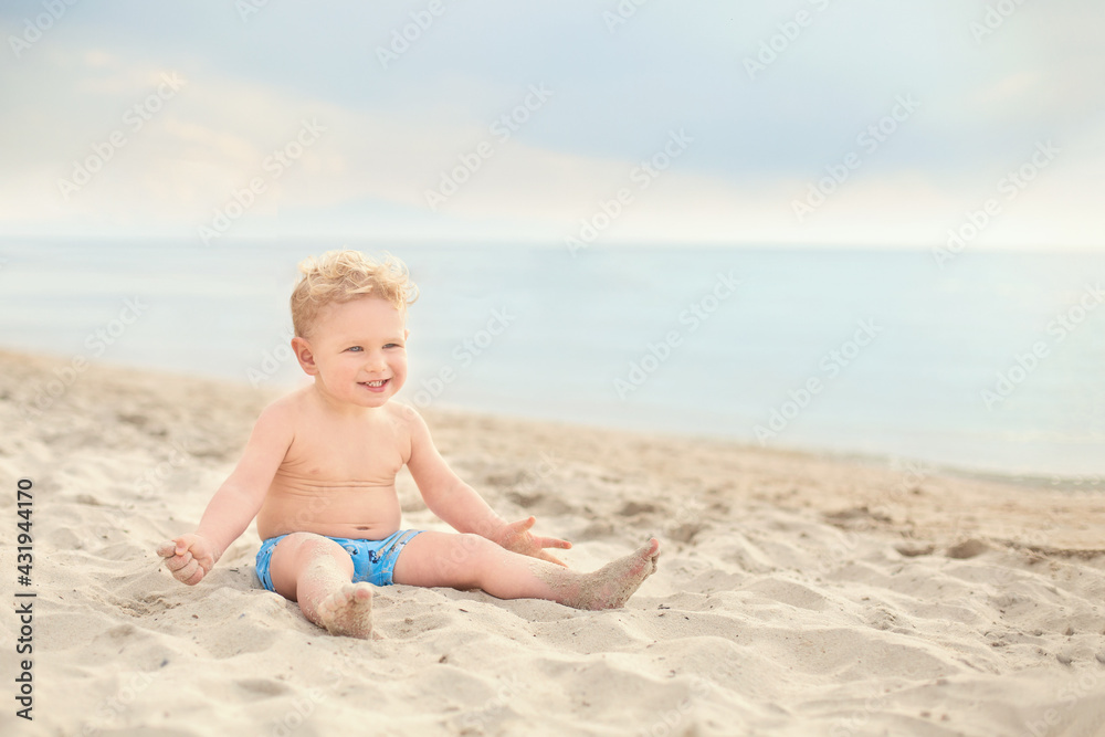one caucasian blond toddler boy sitting smiling seashore. Summer vacation, sea holidays, outdoor leisure time, play outdoors, healthy time, happy childhood concept. one caucasian blond toddler boy sitting smiling seashore. Summer vacation, sea holidays, outdoor leisure time, play outdoors, healthy time, happy childhood concept.