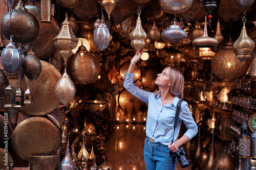 Travel and shopping. Young traveling woman with choose presents in copper souvenir handicraft shop in Morocco.