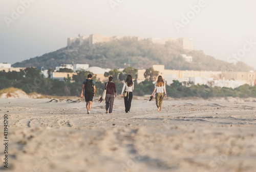 Friends walk on the beach on a sunny day. Back view. Castle and old town in the background.