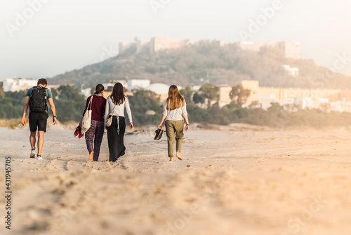 Friends walk on the beach on a sunny day. Back view. Castle and old town in the background.