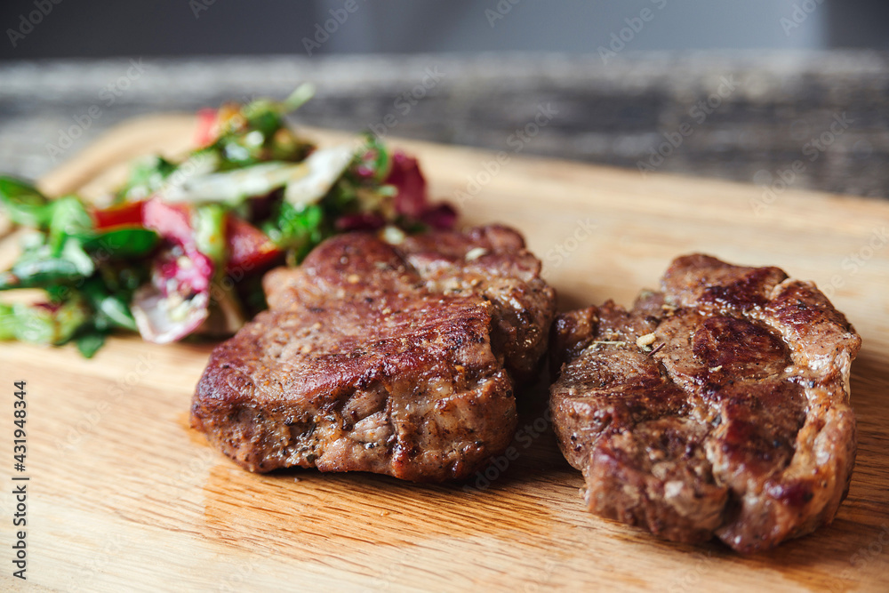 Grilled beef steaks on wooden cutting board. Tasty juicy grilled steak and salad with tomatoes on cutting board.
