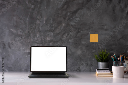 Workspace with white blank on tablet pc, books and tree pot on wood table with living room concrete loft wall