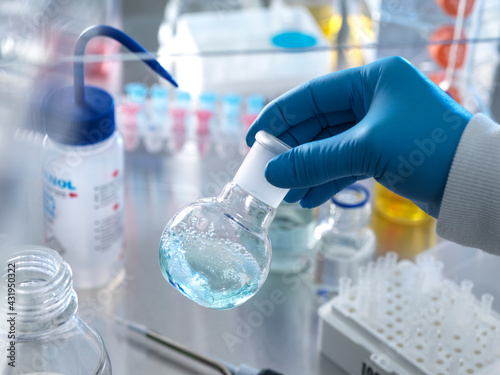 Scientist holding flask containing chemical formula under fume hood in laboratory photo