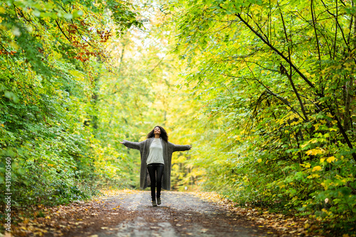 Carefree woman with arms outstretched running on footpath in forest