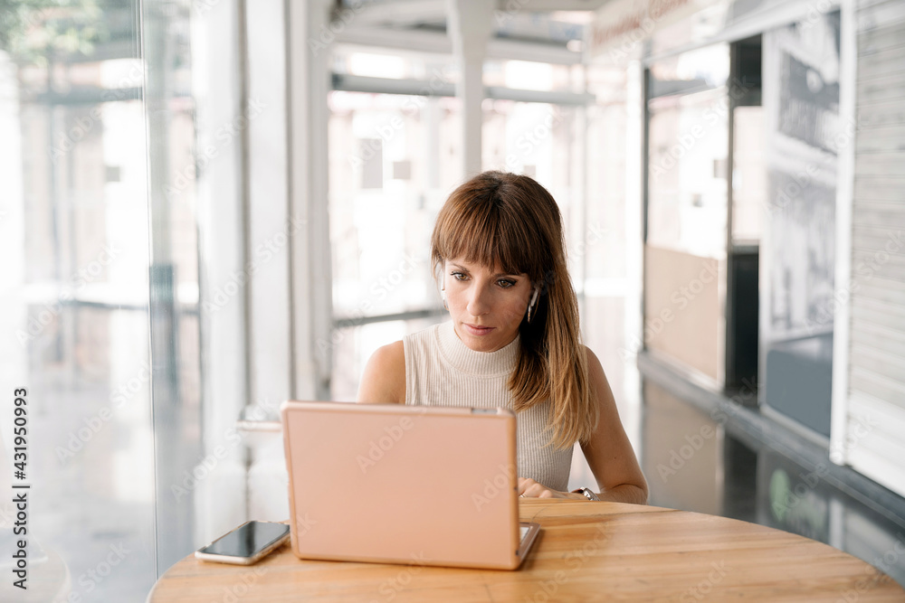 Woman with bangs working on laptop in cafe Woman with bangs working on laptop in cafe