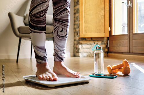 Woman analyzing weight while standing on weight scale at home